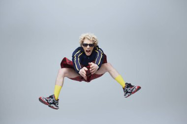 İskoç geleneksel kıyafetleri içinde duygusal, komik bir adam ve gri stüdyo geçmişine karşı havada eski spor kıyafetleri içinde. Moda birleşimi, sanat, tarz, nonoş, eşsizlik, kendini ifade etme kavramı. Ad