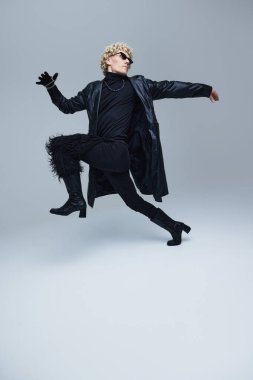 Modern erkeklik. Tamamen siyah giyinmiş genç adamın dinamik portresi gri stüdyo arka planında koşuyor. Moda birleşimi, sanat fotoğrafçılığı, stil, nonoşluk, eşsizlik kavramı. Ad