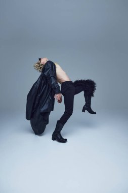 Siyah pantolonlu, topuklu ayakkabılı, sanatsal dans figüründe geriye doğru kıvrılan üstsüz bir adam gri stüdyo arka planına karşı. Moda birleşimi, sanat, tarz, nonoş, eşsizlik, kendini ifade etme kavramı. Ad