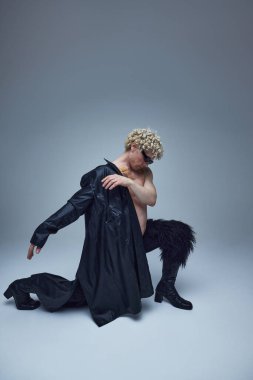 Esnek erkek model dramatik dans pozu veriyor. Gri arkaplana karşı poz veren modaya uygun siyahi kıyafetli çekici bir genç. Moda birleşimi, tarz, eşsizlik, kendini ifade etme kavramı. Ad