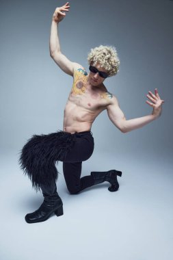 Gri stüdyo arka planında tüylü çizmeleri ve pantolonu olan seksi dans pozu veren ilginç bir adam. Moda birleşimi, tarz, nonoş, eşsizlik, kendini ifade etme kavramı. Ad