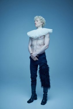 Geçmiş ve şimdiki zaman. Mavi stüdyo arka planında fırfırlı yakalı ve siyah pantolonlu üstsüz bir adamın tam boy portresi. Moda birleşimi, tarz, nonoş, eşsizlik, kendini ifade etme kavramı. Ad