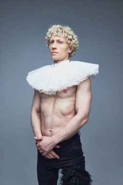 Geçmiş ve şimdiki zaman. Gri stüdyo arka planında fırfırlı yakalı ve siyah pantolonlu üstsüz bir adamın portresi. Moda birleşimi, sanat fotoğrafçılığı, stil, nonoş, eşsizlik, kendini ifade etme kavramı