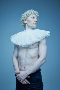 Moda evrimi. Dalgalı yakalı, siyah pantolonlu, mavi stüdyo geçmişine bakan üstsüz bir adamın portresi. Moda birleşimi, tarz, nonoş, eşsizlik, kendini ifade etme kavramı.