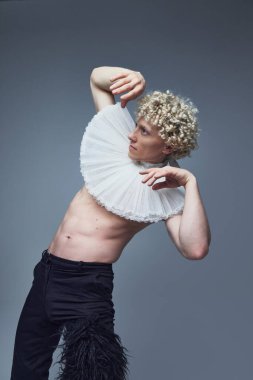 Gri stüdyo arka planına karşı tarihi ve çağdaş modayı düşünceli jestlerle harmanlayan sanatçı erkek model. Moda birleşimi, sanat, tarz, nonoş, eşsizlik, kendini ifade etme kavramı. Ad