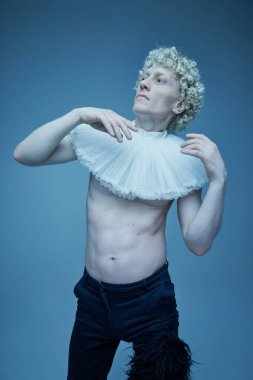 Çağların birleşimi. Süslü yakalı, kıvırcık sarı saçlı ve mavi renkli arka planda desenli pantolonlu dalgın genç bir adam. Moda anlayışı, tarz, eşsizlik, kendini ifade etme. Ad