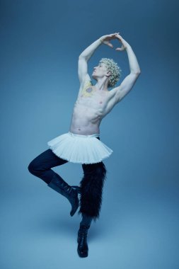 Tişörtsüz bir adam ve bale pozu veren botsuz bir adam. Gri stüdyo geçmişine karşı poz veriyor. Güç ve zarafeti somutlaştırıyor. Moda anlayışı, sanat fotoğrafçılığı, stil, nonoş, eşsizlik, kendini ifade etme. Ad