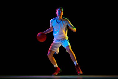 Odaklanmış basketbol oyuncusu, karışık neon ışıkta siyah stüdyo arka planına karşı çift top tekniği uyguluyor. Profesyonel spor kavramı, enerji, güç ve güç, maç, şampiyonluk.