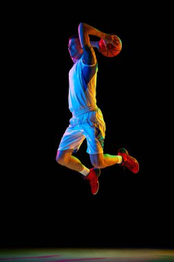 Basketbolcu karışık neon ışıkta siyah stüdyo arka planına karşı basket potaya gidiyor. Dinamik çekim. Profesyonel spor, enerji, güç ve güç kavramı, maç, turnuva.