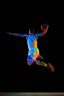 Basketbolcunun dinamik portresi karışık neon ışıkta siyah stüdyo arka planına karşı mükemmel turnike yapıyor. Profesyonel spor kavramı, enerji, güç ve güç, maç, şampiyonluk.