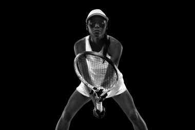 Tenisçinin ön görüntüsü, siyah stüdyo arka planına karşı oynanmasını bekleyen raketi engelliyor. Monokrom filtresi. Kadınların spor anlayışı, aktif yaşam tarzları, turnuvalar, enerji, hareket.