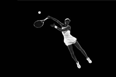 Tenisçinin siyahi stüdyo arkaplanıyla eşleşen hareketli fotoğrafı. Monokrom filtresi. Kadınların spor anlayışı, aktif yaşam tarzları, turnuvalar, enerji, hareket.
