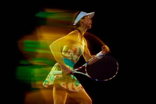 Happy woman, tennis player shouting of joy and clenched hand in fist against black studio background. Motion blur effect. Concept of sport, active lifestyles, tournaments and events, energy, movement.