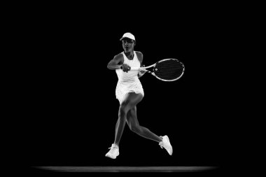 Tenisçinin yukarıdan atlamak için atlarken çekilmiş dinamik fotoğrafı siyah stüdyo arka planıyla eşleşiyor. Monokrom filtresi. Spor anlayışı, aktif yaşam tarzları, turnuvalar ve etkinlikler, enerji, hareket.