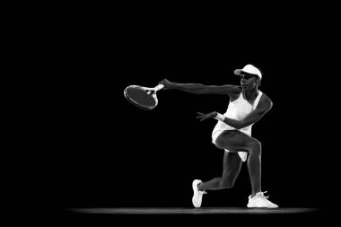 Kadın tenisçinin dinamik portresi siyah stüdyo arka planına karşı forehand dönüş yapıyor. Monokrom filtresi. Kadınların spor anlayışı, aktif yaşam tarzları, turnuvalar, enerji, hareket.