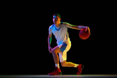 Yetenekli, odaklanmış basketbol oyuncusu karışık neon ışıkta siyah stüdyo arka planına karşı kombine top tutma tekniği uyguluyor. Profesyonel spor konsepti, enerji, maç, şampiyonluk, turnuva