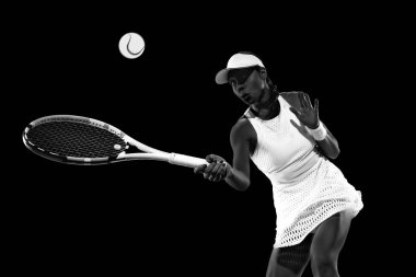 Odaklanmış sporcu, siyah stüdyo arka planına karşı teniste ters vuruş için hazır. Monokrom filtresi. Kadınların spor anlayışı, aktif yaşam tarzları, enerji, hareket.