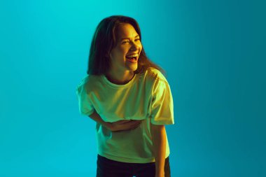 Genç bir kadının portresi elini parlak sarı neon ışıkta uzun kahkahaların karnına koydu. İnsan duyguları kavramı, yüz ifadesi, kendini ifade etme. Ad