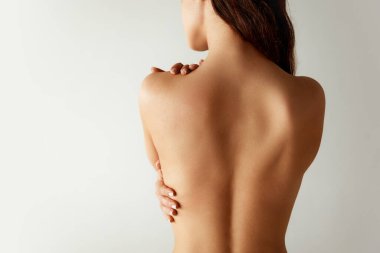 Kapatın. Arka planda, bej iç çamaşırlı yarı çıplak bir kadın gri stüdyo arka planında kendine sarılıyor. Vücut pozitifliği. Güzellik tedavileri, diyet, kadın sağlığı, spa prosedürleri kavramı.