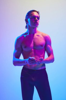 Genç, çekici, yarı çıplak, kaslı vücutlu, parlak neon ışıkta gradyan mavi-pembe arka plana poz veren bir adam. Doğal güzellik insanları, fitness, erkek sağlığı, erkeklik kavramı.