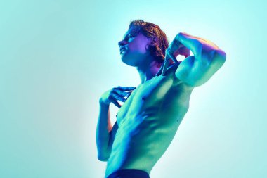 Mükemmel vücut şekilleri olan genç bir adamın mavi arkaplana karşı karışık mavi-mor neon ışıkta poz vermesi. Doğal güzellik insanları, fitness, erkek sağlığı, sağlık, erkeklik kavramı.