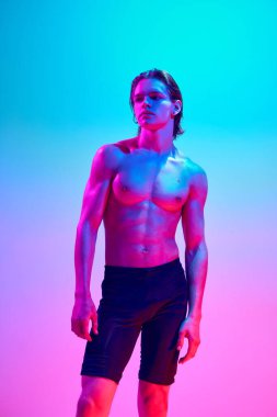 Tişörtsüz genç ve çekici bir adamın portresi parlak neon ışıkta, değişken mavi-pembe arka plana bakıyor. Doğal güzellik insanları, fitness, erkek sağlığı ve refahı, erkeklik kavramı.