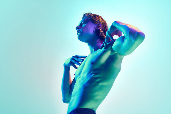 Side view portrait of young man with perfect body shapes posing in mixed blue-purple neon light against blue background. Concept of natural beauty people, fitness, male health, wellness, masculinity.