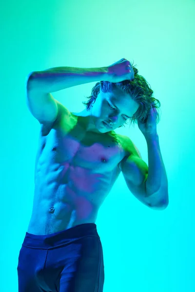 Photo of Shirtless man with sculpted physique posing in mixed cold neon colors against gradient blue background. Concept of natural beauty people, fitness, male health and wellness, masculinity.
