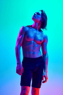 Atletik vücutlu genç bir adamın portresi parlak neon ışıklarıyla siyah kısa poz vererek, gradyan mavi-pembe arka plana karşı. Doğal güzellik insanları, fitness, erkek sağlığı, erkeklik kavramı