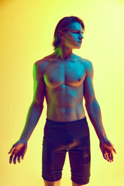 Kendine güvenen erkek modelin portresi sarı stüdyo arka planında yoğun sarı ve yeşil ışıkta poz veriyor. Doğal güzellik insanları, fitness, erkek sağlığı ve refahı, erkeklik kavramı.