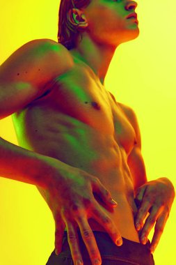 Kusursuz, heykel gibi bir vücudu olan, rengarenk neon ışığı olan, eğimli sarı arka planda bir insan portresi. Doğal güzellik insanları, fitness, erkek sağlığı ve refahı, erkeklik kavramı.