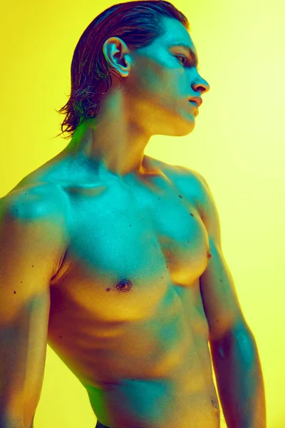 Creative portrait of male model posing in vibrant blue neon light against gradient yellow background. Strong male figure highlighted by glow. Concept of natural beauty, male health, masculinity.