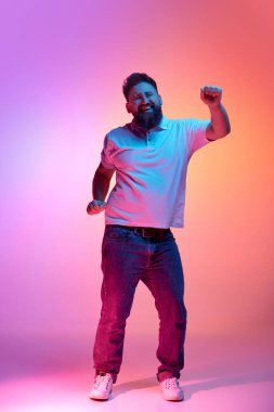 Sakallı, günlük kıyafetli, neon ışıkta dans eden genç bir adamın tam boy portresi. İnsan duyguları, kendini ifade etme, güzellik ve moda kavramı. Ad