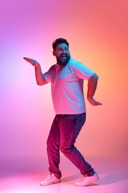 Mutluluk dansı. Neşeli yüzüyle neon ışıklarıyla dans eden gündelik kıyafetli bir adam canlı gradyan stüdyo arkaplanına karşı. İnsan duyguları, kendini ifade etme, güzellik ve moda kavramı. Ad
