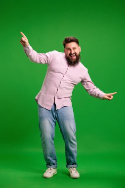 Canlı yeşil stüdyo arka planında dans eden genç adamın tam boy portresi. Başarı zamanı. İnsan duyguları kavramı, kendini ifade etme, dinlenme, hobiler, boş zaman.