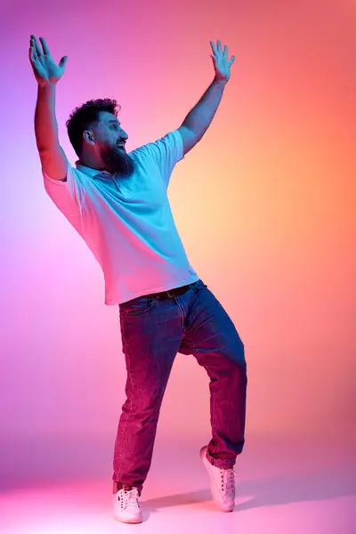 stock image Young overjoyed man waving hands while dancing in motion in neon light against vibrant gradient studio background. Concept of human emotions, self-expression, fun and joy, beauty and fashion. Ad