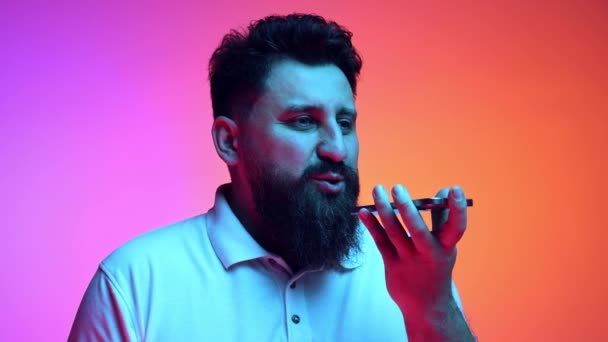 男人在霓虹灯下对着渐变的粉色橙色工作室背景 一边拿着电话一边说话 人类情感的概念 自我表达 距离的联系 — 图库视频影像