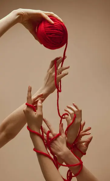 Friendship. Hand holds ball of threads and hands nearby unravel this tangle, intertwining and uniting against sandy color studio background. Concept of human touch, beauty and care, spa procedures.