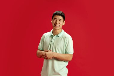 Genç, yakışıklı, sıradan giyinen Asyalı adam kırmızı stüdyo geçmişine gülüyor. Olumlu duygular. Mizah ve komedi anlayışı, moda ve güzellik, kendini ifade etme, iş ve hobi.