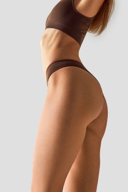 İç çamaşırlı kadın profili, sağlıklı yaşam tarzını gri stüdyo geçmişiyle karşılaştırmak için güçlü, tonlu bir vücudu ön plana çıkarıyor. Güzellik tedavileri, diyet, kadın sağlığı, spa prosedürleri kavramı.