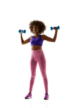 Dambılı gülümseyen kadın, mor spor sutyen giyiyor ve beyaz stüdyo arka planında tayt giyiyor. Spor anlayışı, yas tutma alışkanlığı, aktif ve sağlıklı yaşam tarzı, enerji, eylem.