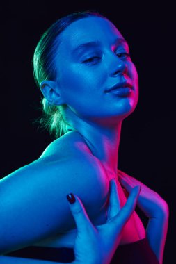 Genç, güzel bir kadının portresi. Dokunaklı omuzlar. Siyah stüdyo arka planında neon ışıkta kameraya bakıyor. Spa prosedürleri, kozmetoloji, yaşlanma ve cilt bakımı ürünleri kavramı. Ad