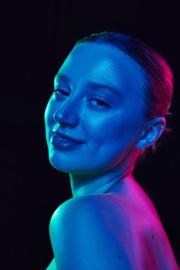 Siyah stüdyo arka planına gülümseyen, neon ışıkta gülümseyen genç ve çekici bir kadın. Parlak cildi olan bir model. Spa prosedürleri, kozmetoloji, cilt ürünleri kavramı