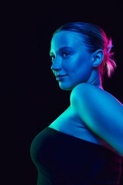 Siyah stüdyo arka planına karşı neon ışıkta poz veren çekici bir kadının düşük açılı görüntüsü. Sağlık konsepti, spa prosedürleri, kozmetoloji, yaşlanma karşıtı ürünler ve cilt bakımı. Ad