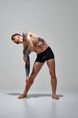 Çekici, dövmeli, atletik vücutlu, iç çamaşırlarıyla poz veren, gri stüdyo geçmişine karşı kollarını kaldıran adam. Uzayı kopyala Doğal güzellik, moda ve tarz kavramı, erkek sağlığı ve vücut bakımı. Ad