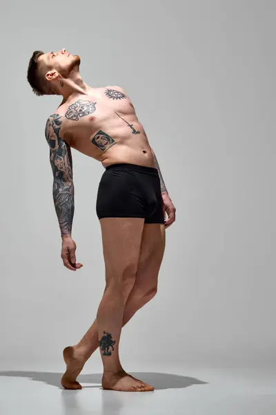 年轻的运动员穿着内衣 在灰色的工作室背景下摆出姿势 身上有纹身的男模复制空间 自然美 时尚与时尚 男性健康与身体护理的概念 免版税图库图片