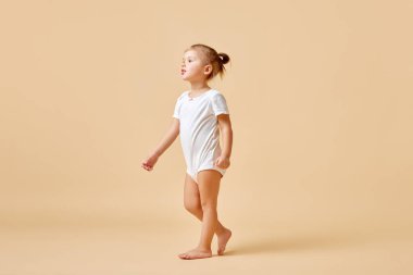 İlk adım. Şirin romper giymiş küçük bir kızın uzun bir portresi. Eğlen ve pastel renkli arka planda koş. Mutluluk kavramı, çocukluk, annelik, yaşam, doğum. İlan için alanı kopyala