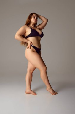 Siyah iç çamaşırlarıyla poz veren çekici, kendine güvenen genç bir kadın. Bikini, gri stüdyo geçmişine bakıyor. Doğal güzellik kavramı, kadınlık, vücut pozitifliği, diyet, fitness.