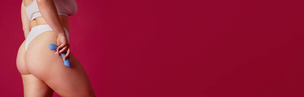 Banner. Young woman hold toy for adult near hip against vibrant pink studio background with negative space to insert text. Concept of toys for adults, pleasure and enjoyment, sensuality.