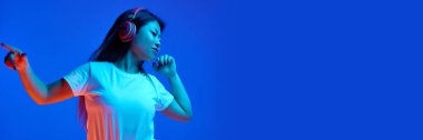 Pankart. Kulaklıkla müzik dinleyen Asyalı kadın mavi ışık altında arka planda. Metin eklemek için negatif boşluk. İnsan duyguları kavramı, kendini ifade etme, dans ve müzik, eğlence, neşe.